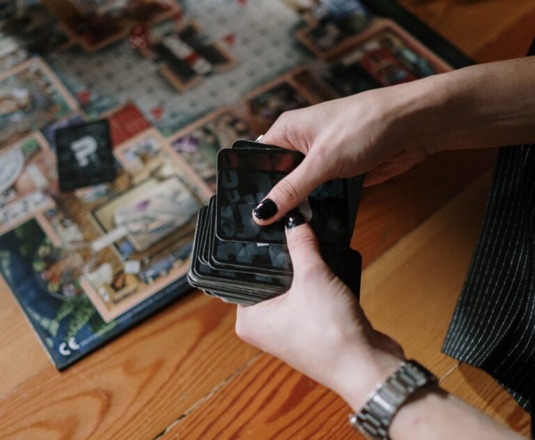 Hands holding cards during a board game session on a wooden floor indoors.