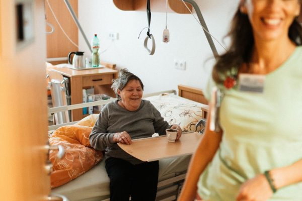 Smiling nurse assists senior patient in a cozy hospital room, promoting healthcare and wellbeing.