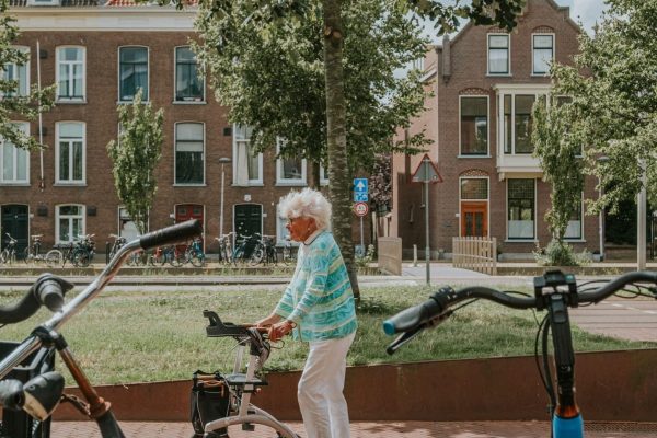 Senior woman strolls with rollator on a sunny day in a Dutch neighborhood surrounded by bicycles.