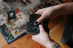 Hands holding cards during a board game session on a wooden floor indoors.