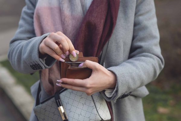 Close-up of a woman placing a coin into a wallet while outdoors, wearing a coat and scarf.